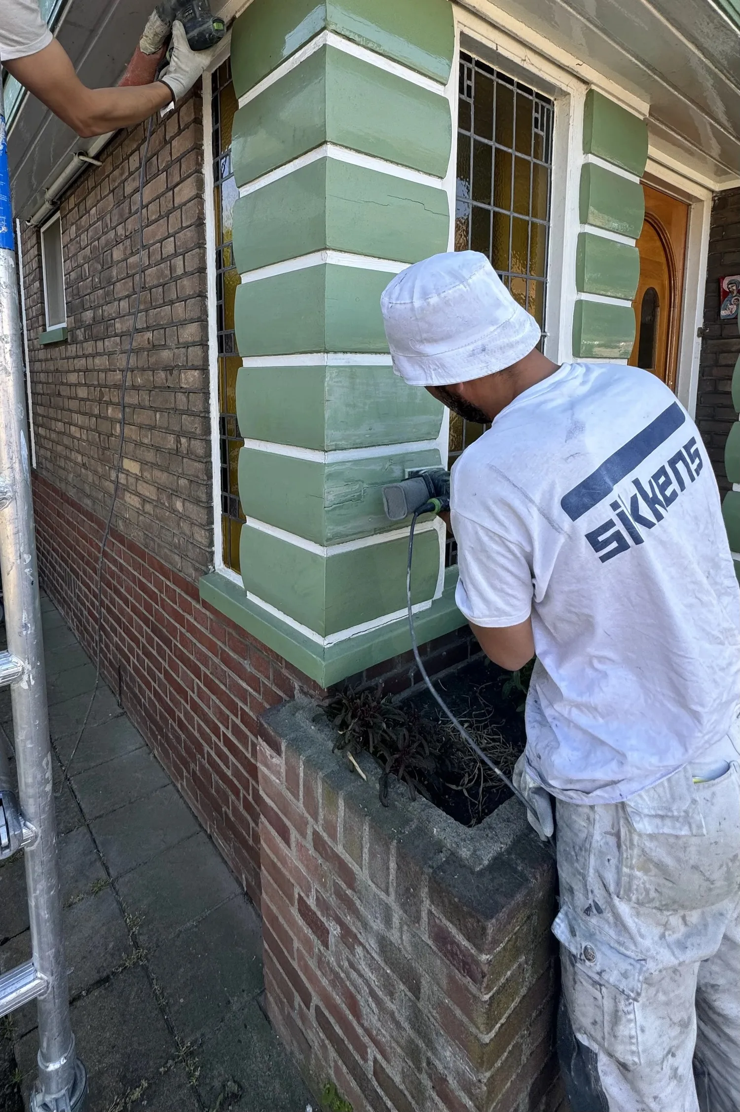 Twee schilders van Diamant schuren het houtwerk van een gevel